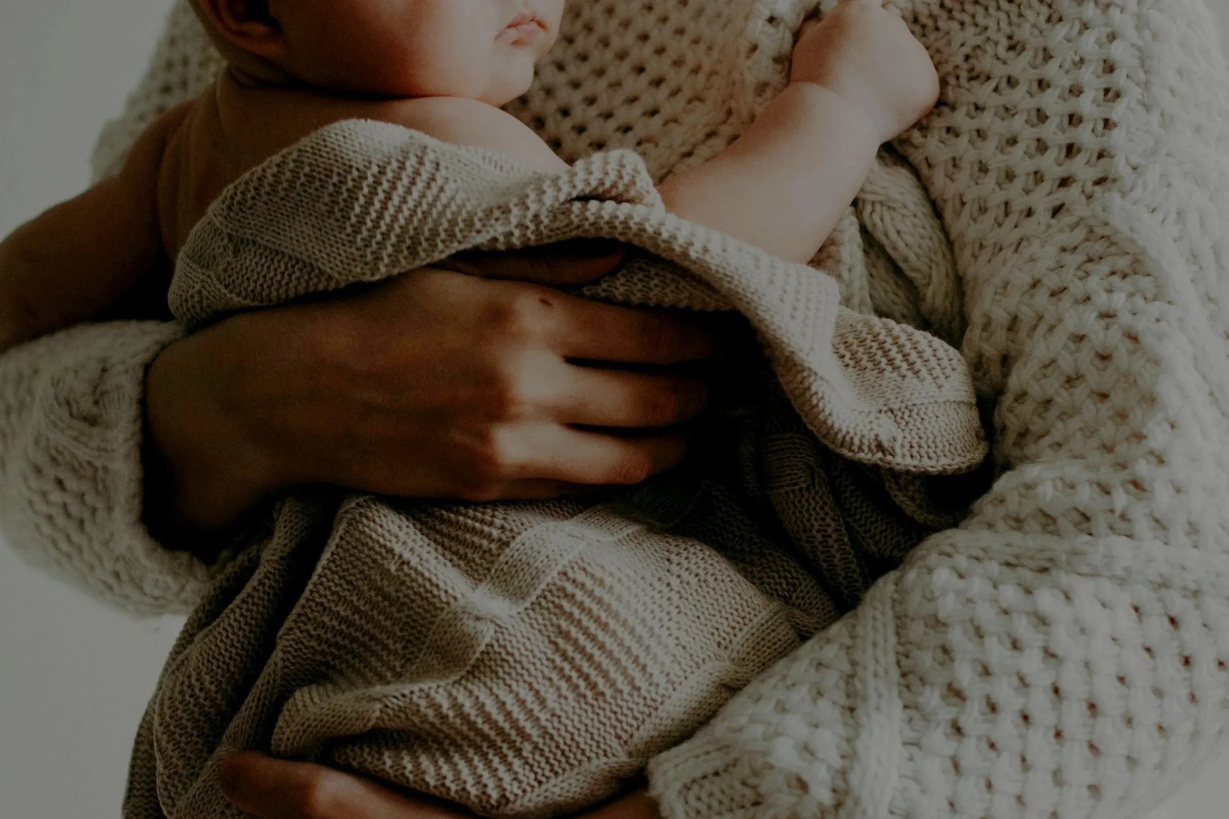 Parent gently holding a newborn wrapped in a soft knit blanket, representing the fertility journey supported by Mighty River Wellness
